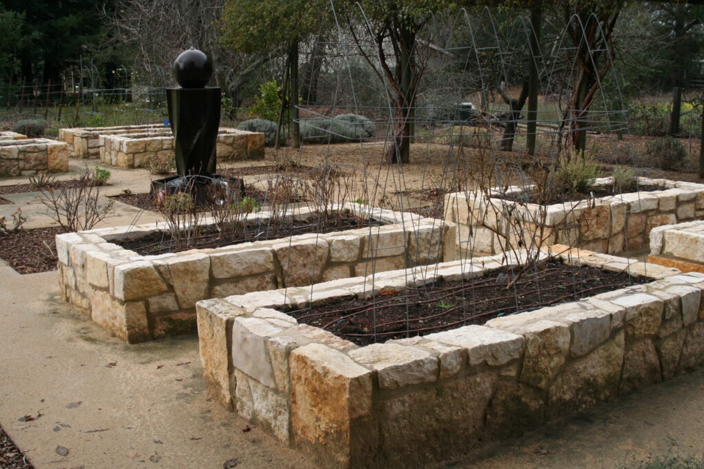 multiple raised planters in a gravel patio; the planters feature cut stone veneer; the planters are currently filled with dead bushes