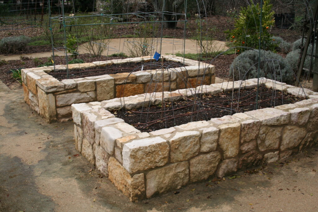 multiple raised planters in a gravel patio; the planters feature cut stone veneer; the planters are currently filled with dead bushes