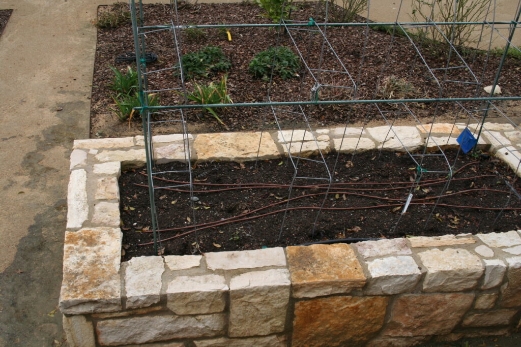 multiple raised planters in a gravel patio; the planters feature cut stone veneer; the planters are currently filled with dead bushes