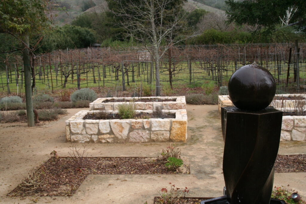 multiple raised planters in a gravel patio; the planters feature cut stone veneer; the planters are currently filled with dead bushes