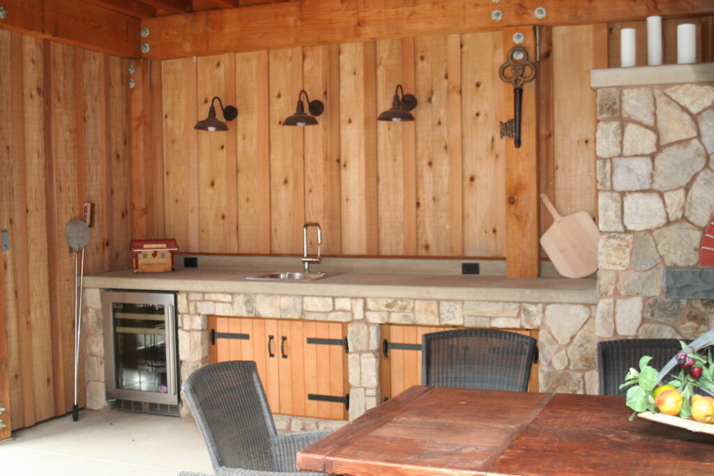 outdoor kitchen features a small utility sink; the counter is made from poured concrete; the cabinets are set into cut stone veneer