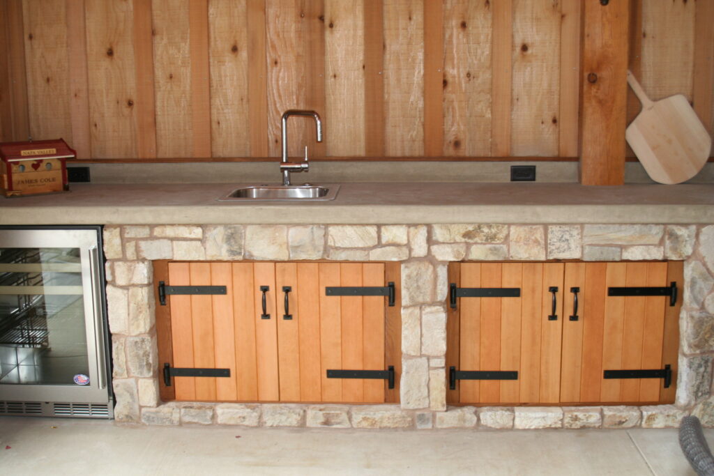 outdoor kitchen features a small utility sink; the counter is made from poured concrete; the cabinets are set into cut stone veneer