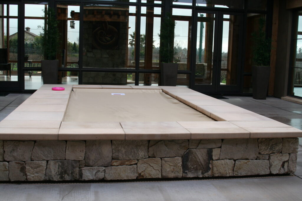 a planter featuring cut stone walls with large tile treads sits in the center of a outdoor patio; the planter is empty and brown paper covers the interior of the planter