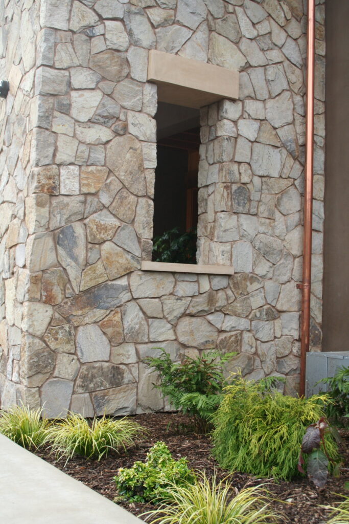 closeup of cut stone facade of a winery; a copper utility pipe rises from the ground to the rooftop