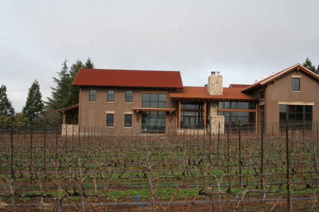 a winery with accents of cut stone veneer stands in the background; before it, grape vines out of season