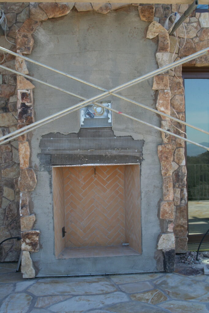 cut stone veneer of the exterior of a chimney; the chimney serves both an indoor and outdoor fireplace; the outdoor fireplace features herringbone laid bricks