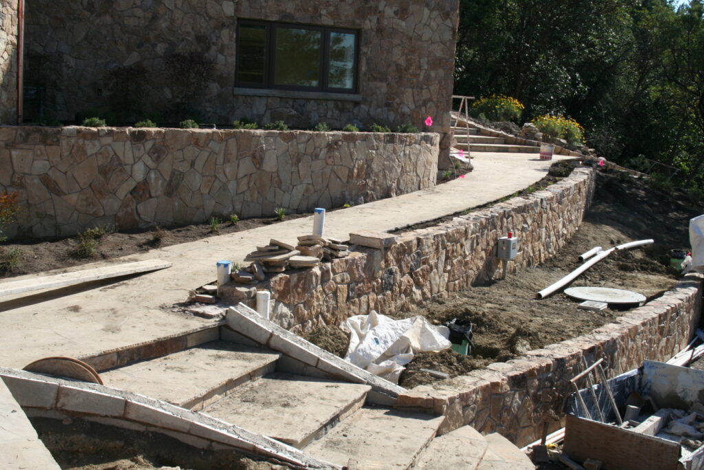 cut stone steps with single stone treads lined on either side by cut stone walls leads up a hill through a tiered garden with exposed irrigation