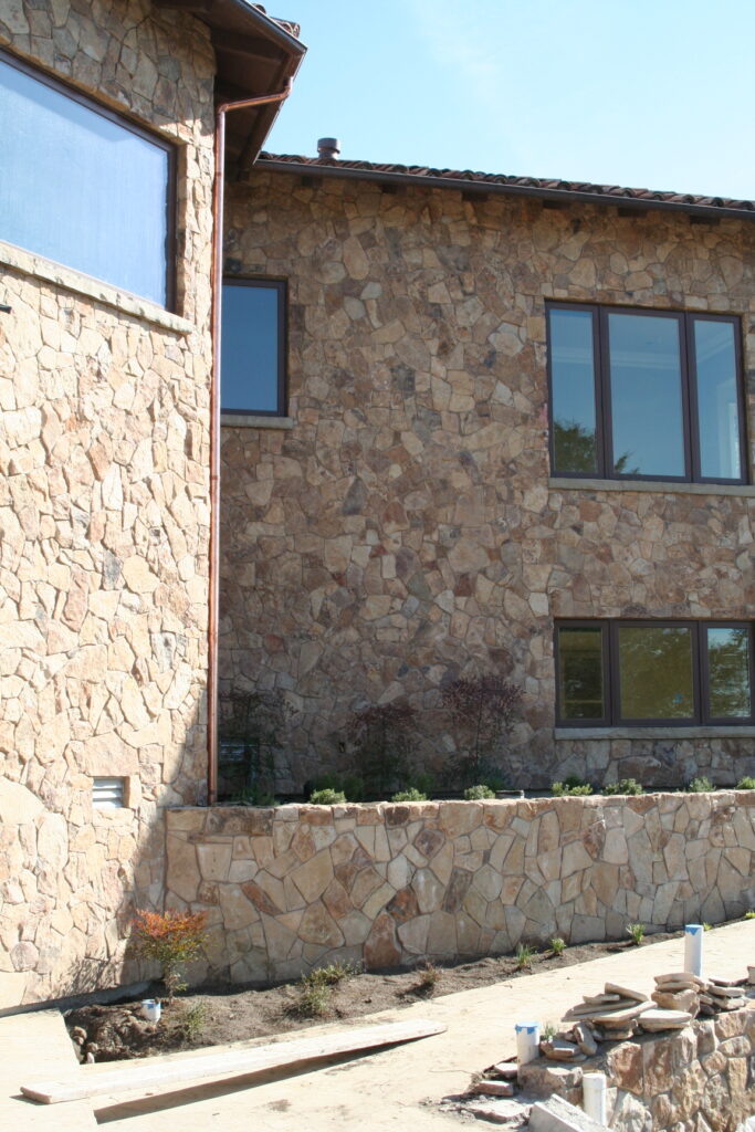 exterior of a building features seamless cut stone veneer that matches the garden planters just outside the building; the windows have bronze metal accents