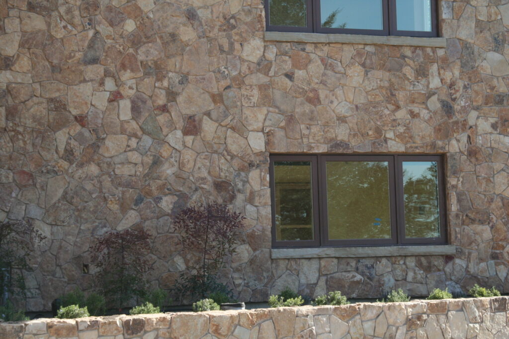 exterior of a building features seamless cut stone veneer that matches the garden planters just outside the building; the windows have bronze metal accents