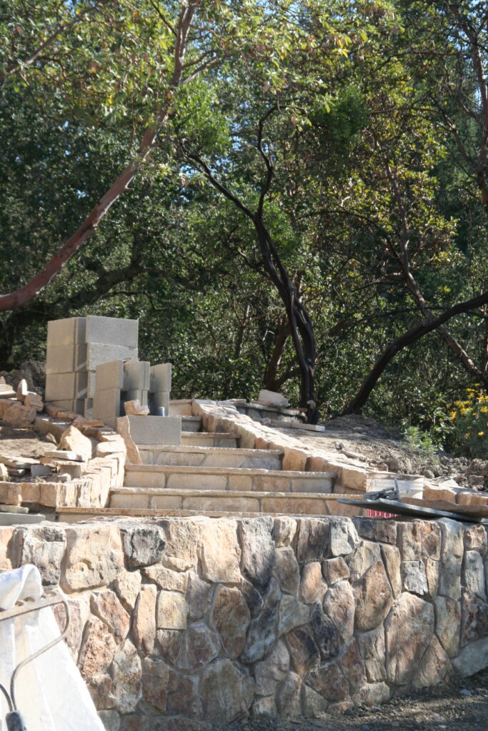 cut stone steps with single stone treads lined on either side by cut stone walls leads down a hill through a tiered garden with exposed irrigation