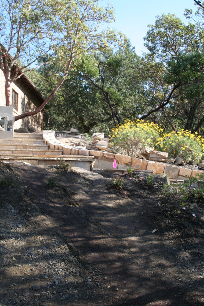 cut stone steps with single stone treads lined on either side by cut stone walls leads down a hill through a tiered garden with exposed irrigation