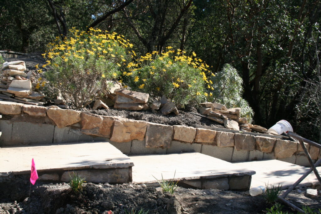 cut stone steps with single stone treads lined on either side by cut stone walls leads down a hill through a tiered garden with exposed irrigation