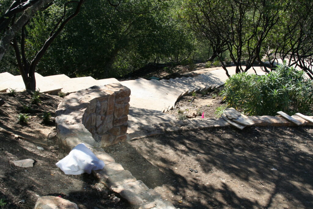 cut stone steps with single stone treads lined on either side by cut stone walls leads down a hill through a tiered garden with exposed irrigation