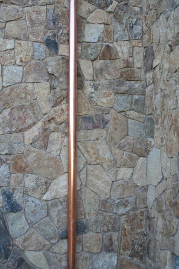 closeup of a copper utility pipe in front of the cut stone veneer of a building