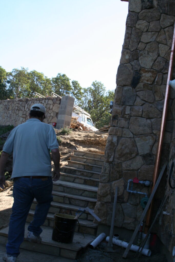 Conrad walks up a cut stone stairway with stone treads; the stairway hugs the outside of a building still under construction