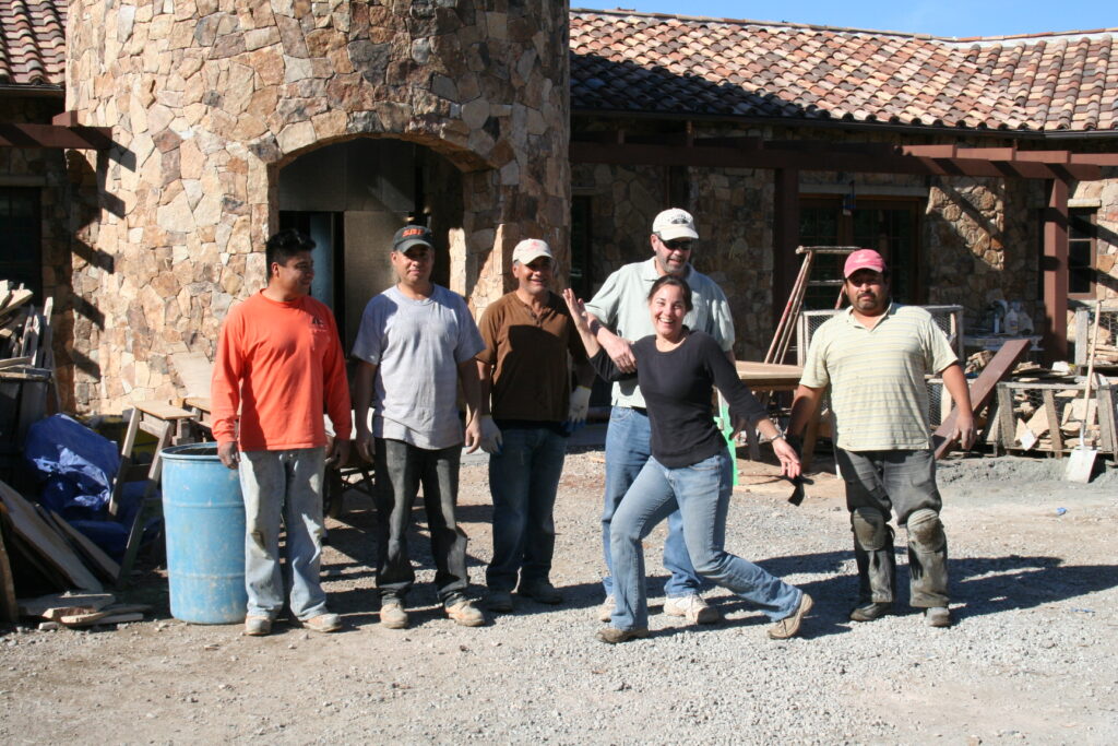 Conrad poses with his professional masonry team outside the front door of an estate still under construction; the facade of the building is covered in cut stone veneer