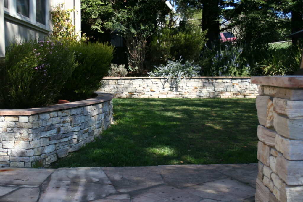 cut stone veneer retaining wall, planters and cute stone walkway surrounding a tiered front yard landscape