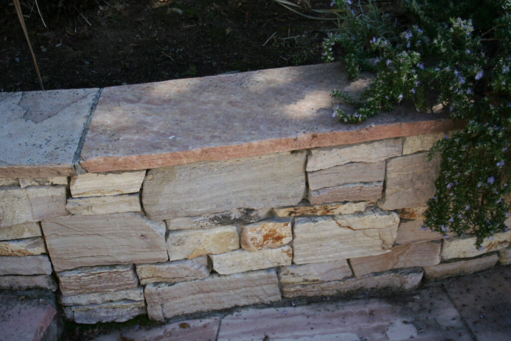 cut stone veneer for a retaining wall with rosemary bush draping over the ledge