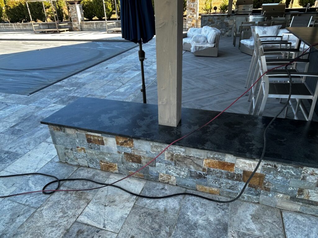 outdoor kitchen with 2 built-in grills; the counters are supported by stone walls; the floor of the outdoor kitchen is laid with stone tiles set in a herringbone pattern