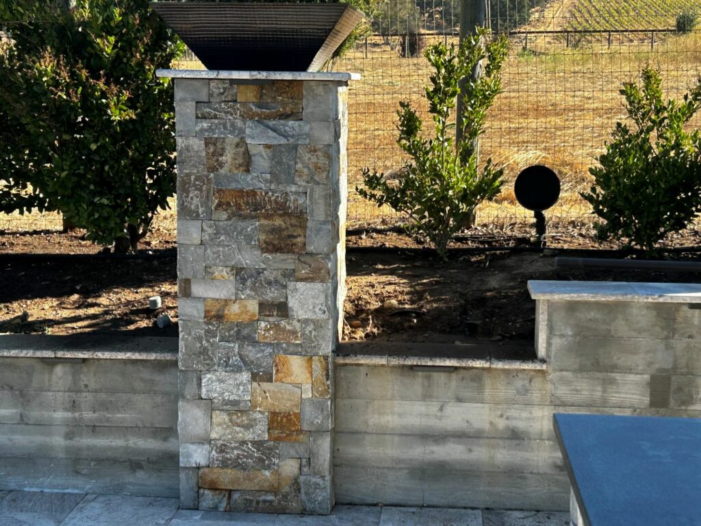 closeup of a stone plinth featuring cut stone veneer; an iron planter rests atop the plinth